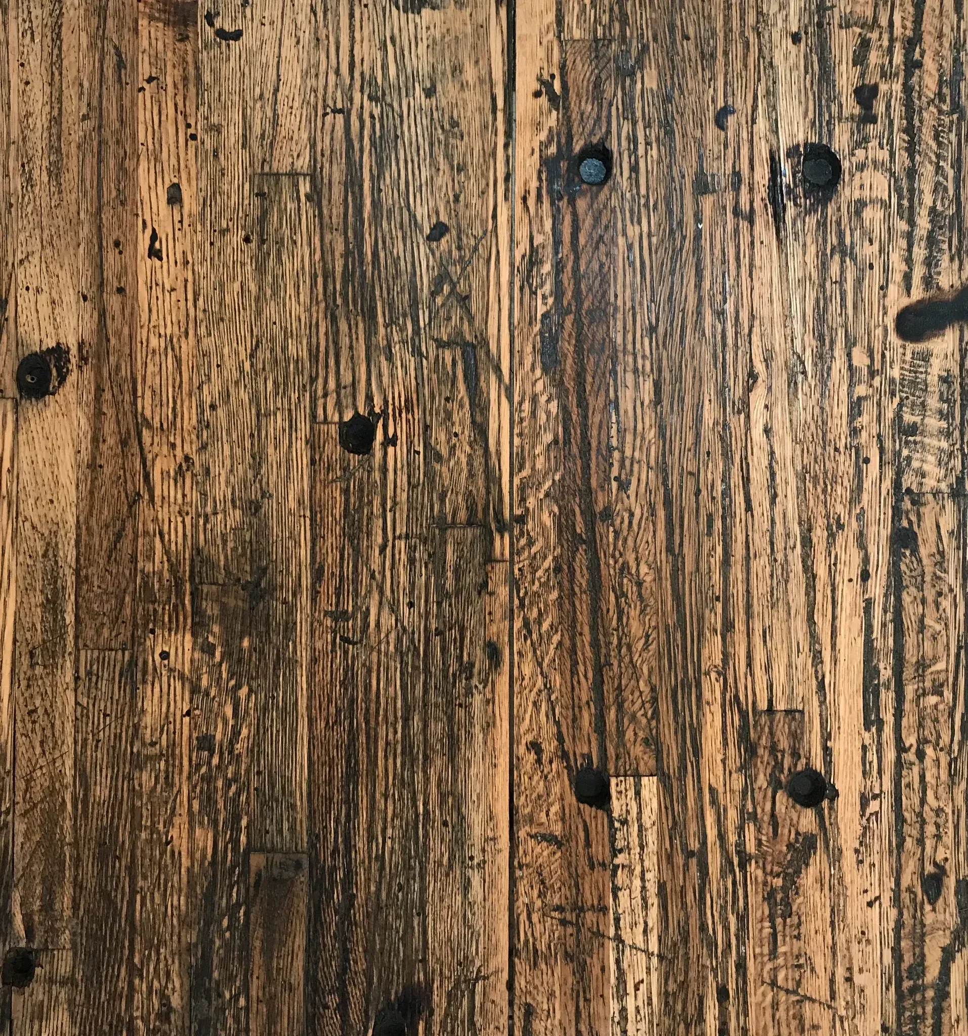 Close-up of a rustic wooden surface with visible grain and dark knots. The wood has a warm, natural color with varying shades of brown, giving it a textured and aged appearance.