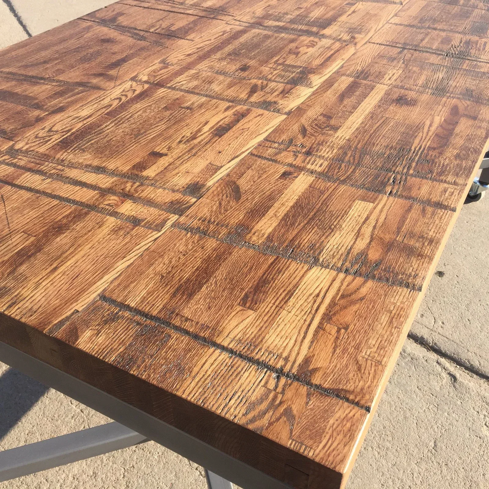 A Reclaimed Rail Car Plank table with a polished surface showcases a geometric pattern of rectangular planks. It stands on metal legs, and the sunlight in the photo beautifully highlights its wood grain and texture.