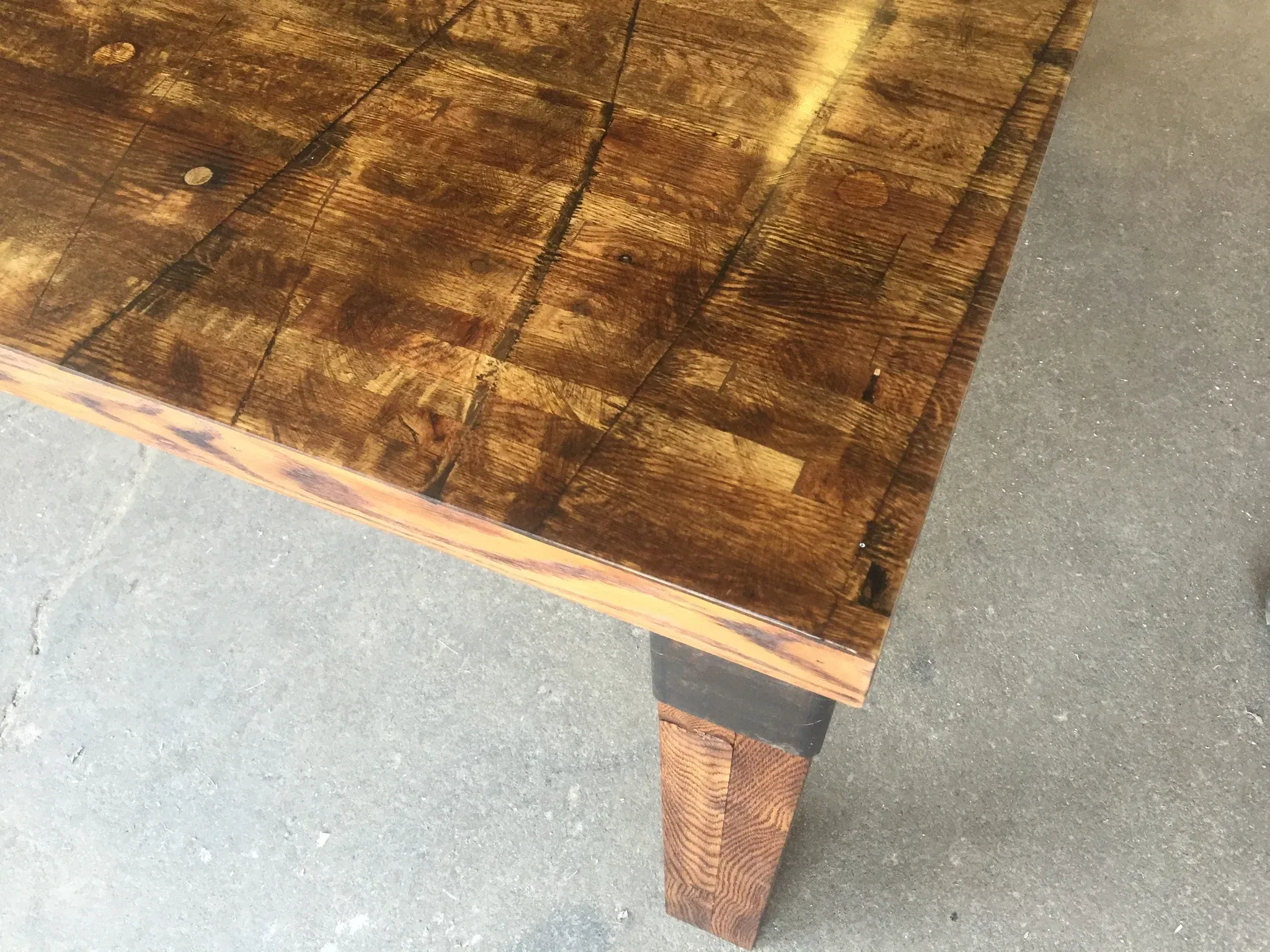 Close-up of the Reclaimed Rail Car Plank, showcasing its rustic, weathered surface with natural wood grain and knots. It sits on a gray cement floor, emphasizing its sturdy construction and simple design.