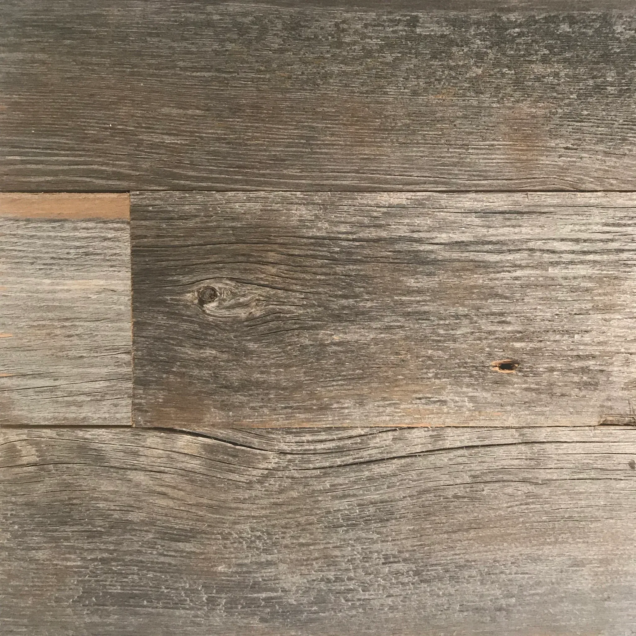 A close-up of Wall & Ceiling Accent Plank featuring a weathered gray and brown wooden surface. The visible wood grain displays natural variations and knots, adding a rustic texture.