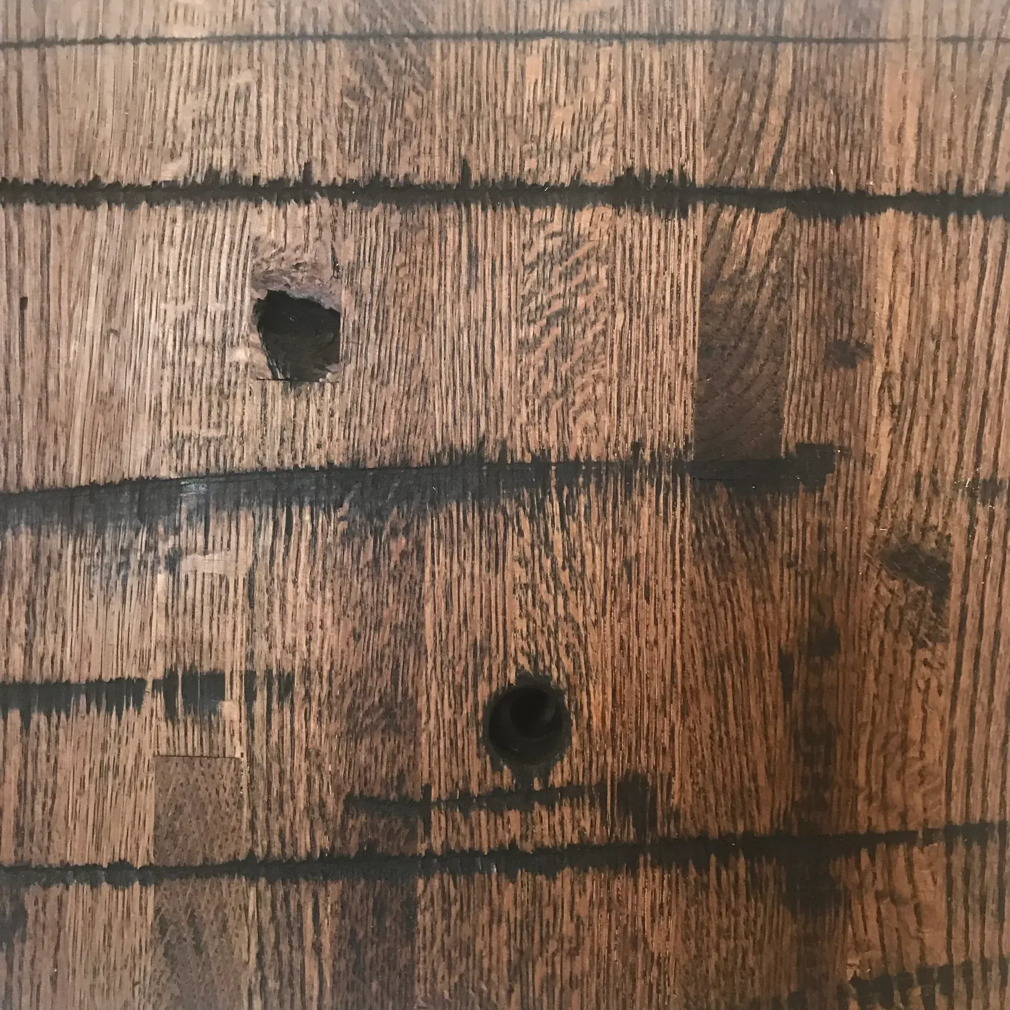 A close-up of the Reclaimed Rail Car Plank, displaying its rustic wooden surface adorned with visible wood grain and two round, dark holes, enhances its weathered and aged look. The plank showcases a warm, natural tone.