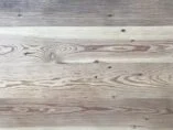 A wooden surface with visible grain patterns and natural variations in color. The wood displays a mix of light and dark tones, with some knots and lines running horizontally across the surface.