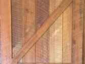 A rustic wooden barn door with vertical planks and a diagonal brace forming a Z pattern. The door displays a natural wood grain and warm brown tones, giving it a vintage, handcrafted appearance.