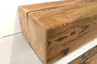 Close-up of a Reclaimed Wood Mantel mounted horizontally on a white wall, its rustic charm highlighted by visible grain, natural weathered texture, and knotholes. The floor beneath enhances the scene with its wooden finish.
