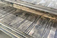 A stack of Reclaimed Rail Car Plank boards with visible grain and cut marks lies on a surface, showcasing a weathered appearance with natural textures and shades of brown and gray.