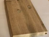 Wooden plank with two round indentations on the surface, placed on a light-colored surface. The plank has visible grain patterns and a rectangular shape.