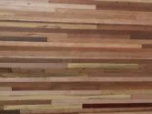 A wooden wall with horizontal strips of various shades and textures, ranging from light tan to dark brown. The different wood grains and colors create a natural, rustic pattern.