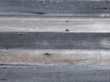 A close-up of weathered wooden planks arranged horizontally. The wood features varying shades of gray and brown, with visible grain and knots, giving it a rustic and aged appearance.