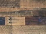 Close-up of weathered wooden planks with varying shades of brown and gray. The boards have visible grain patterns, knots, and some small imperfections, creating a rustic texture and appearance.